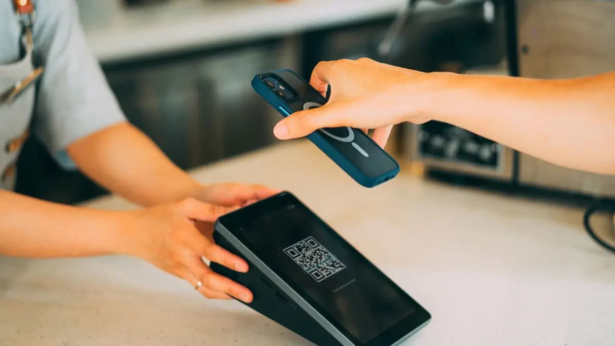 Casieră dintr-un magazin de proximitate care înmânează bonul fiscal unui client care ține telefonul în mână